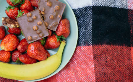 Summer set: strawberries, banana and chocolate on a plaid in a plate. summer picnic checkered bedspread. place for textの写真素材