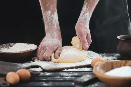 Beautiful and strong men's hands knead the dough from which they will then make bread, pasta or...
