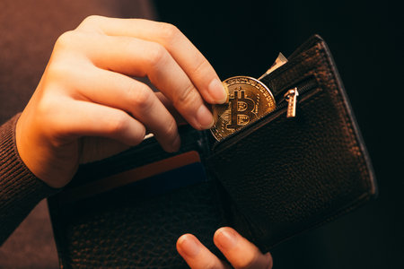 Woman putting golden bitcoin into her wallet on light background, closeup