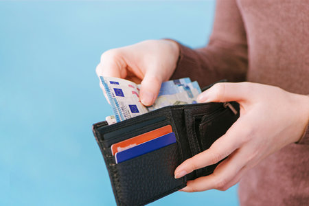 A woman takes out money from a wallet on a blue background with a place for text. payment concept.の写真素材
