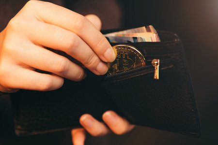 Hand putting golden bitcoin into her wallet on dark background, close up.