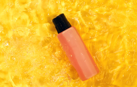 Shower gel or shampoo in a pink bottle on a yellow background with splashes and drops of water, top view. Body and hair care concept, summer cosmetics.の写真素材