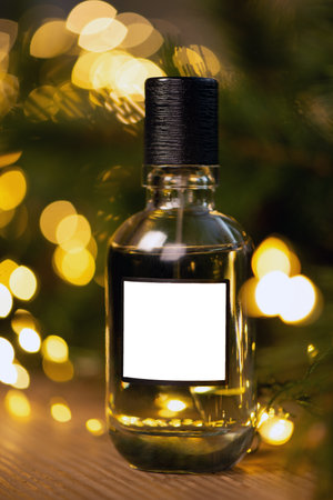 Beautiful composition of a bottle of perfume on a wooden table against the background of garland lights and branches of a Christmas tree. New year gift, holiday concept. Mock upの写真素材