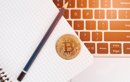 Laptop of bitcoin miner. Bitcoin golden coin on a keyboard and on a notebook with a pencil. Business. top view.の写真素材