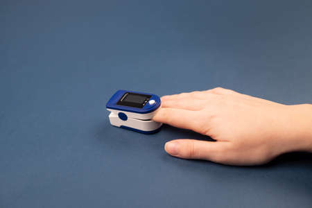 Hand with a finger in pulse oximeter on dark blue background. Self monitoring and protection during pandemic concept. Copy spaceの写真素材