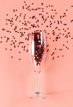 A glass of champagne filled with stars confetti on a pink pastel background. Top view. card blank. Copy space and vertical orientationの写真素材