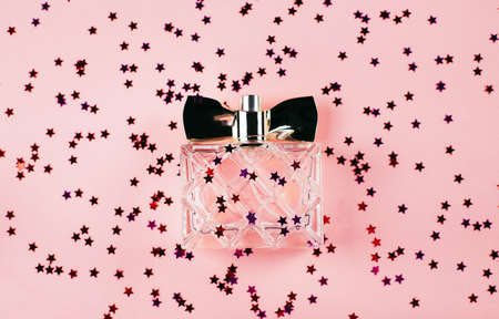 A bottle of women's perfume on a festive pink background with multi-colored sparkles and confetti. view from above. holiday concept february 14 or march 8.の写真素材