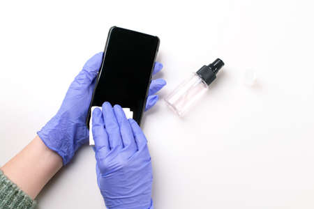 Hands in rubber gloves wipe the phone with disinfectant on a white background. Copy space. Hygiene for the prevention of  virus. Health care conceptの写真素材