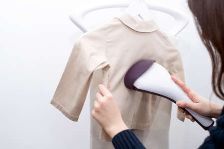 Woman using steaming iron to ironing shirt in laundry room. Girl doing stream vapor iron for press...