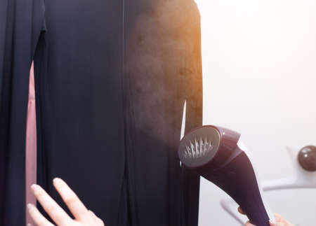 Woman using steaming iron to ironing shirt in laundry room. Girl doing stream vapor iron for press...