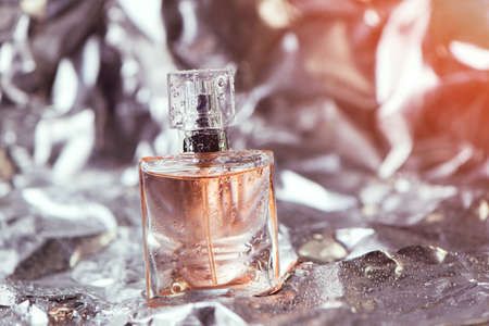 Stylish bottle of women perfume on the foil with shiny crumpled surface silver background with water drops. selective focusの写真素材