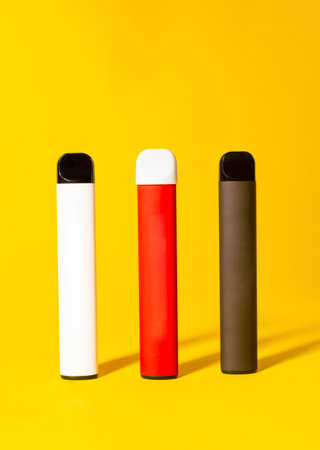 Colorful disposable electronic cigarettes with shadows on a yellow background. The concept of modern smoking, vaping and nicotineの写真素材