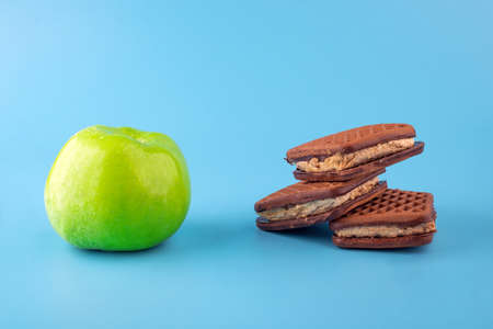 Deciding what to choose. chocolate chip cookie and green apple on blue background. Hard choice between healthy and unhealthy food. Sweet temptation fitnessの写真素材