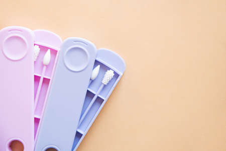 Reusable silicone ear sticks in colored cases with a top view on a beige background. An alternative to disposable cotton swabs. Reduce costs and save money.の写真素材
