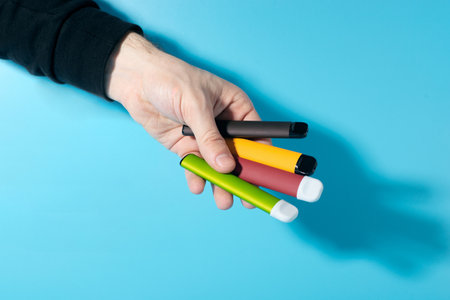 Disposable electronic cigarettes in hand closeup on a blue background with shadows. The concept of...