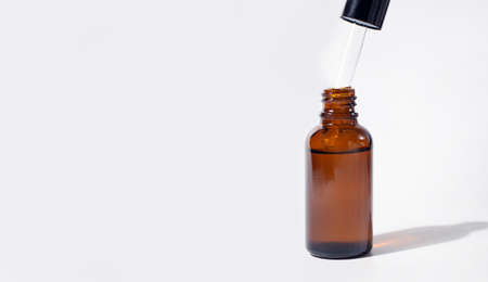 Cosmetic pipette with drops of oil or serum with shadow. Transparent brown bottle. Close up, copy space, banner. Gray background. Health, skin, body care. Aromatherapyの写真素材