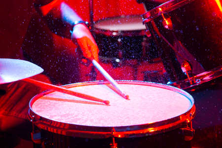 man playing the snare drum on a beautiful colored background, the concept of musical instruments with splashing water on dark background with red studio lighting. Dynamic scene.の写真素材
