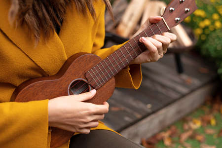 girl closeup playing an acoustic instrument ukulele in autumn on the terrace