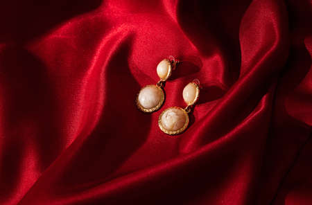 Women's earrings on red silk background. Round golden earrings close-up. Elegant woman jewelry,の写真素材