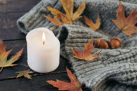 Cozy and autumnal atmosphere. A candle is burning against the background of a knitted blanket with...
