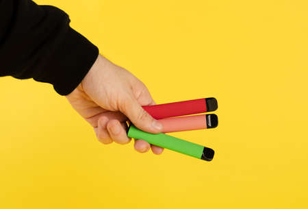 Disposable electronic cigarettes of different flavors in hand on a yellow background. The concept of...