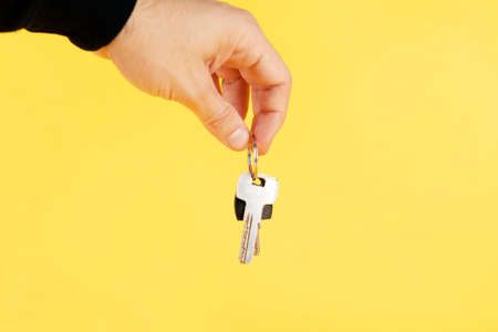 hand holding house keys, suggesting, over yellow background.の写真素材