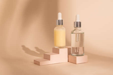 Glass cosmetic bottles with oil or serum for skin care on stone podium on beige background with hard shadows. Natural skin care concept. Oily cosmetic pipette.の写真素材