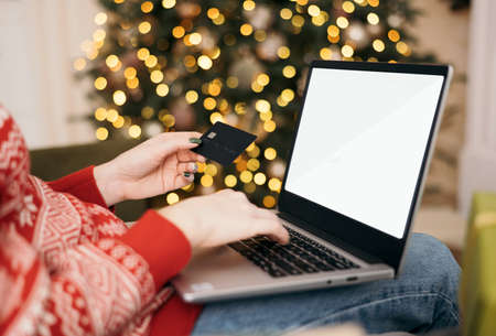 Christmas online shopping, sales and discounts promotions during winter holidays, online shopping at home. Mock-up. Female hands on the laptop with credit card and blurred bokeh lightsの写真素材