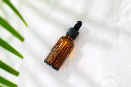 Bottle serum, oil cosmetic in clean transparent water and green leaves. with shadows and waves on...