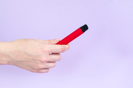 Disposable electronic cigarette of various flavors in hand on a Light Violet background. The concept of modern smokingの写真素材