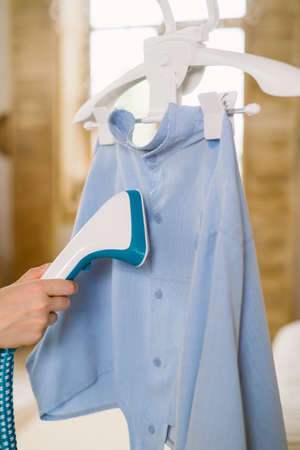 Using steaming iron to ironing shirt in home. Doing stream vapor iron for press clothes in hand. . high quality photoの写真素材
