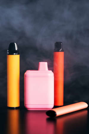 A set of colorful disposable electronic cigarettes of different shapes on a black background with smokeの写真素材