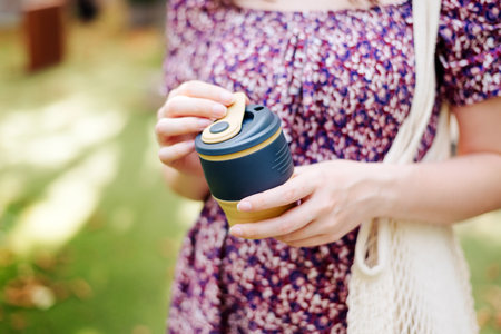 Young female in dress holding reusable silicone foldable coffee tea mug close-up. eco friendly. mesh...