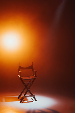 The director's chair stands in a beam of light with an orange backlight and smoke. Place for text. free chair. Concept of selection and casting. shadow and lightの写真素材