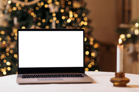 Front view of white screen laptop in home with christmas tree and warm light candle. remote work. Black Friday deals. online shopping. Gifts for the new year and christmasの写真素材