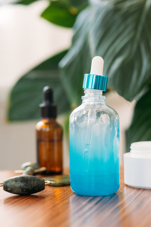 Essential aroma oil or serum essence in blue glass bottle s on a wooden table against a background of green plants and beauty products. Concept of cosmetology, medicineの写真素材
