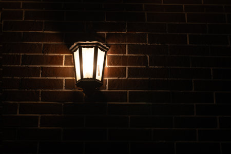 Retro-style lamp hangs on a red brick wall at night, copy space.の写真素材