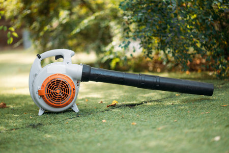 A close-up of an orange cordless, electric leaf blower lying on a grass. Autumn, fall gardening...