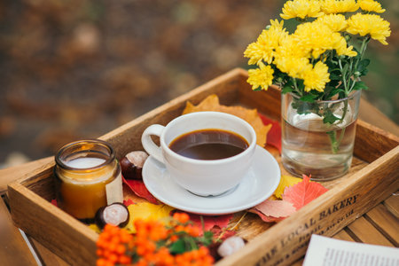 A cup of tea or coffee on a wooden tray against the background of fallen leaves, candle, autumn season, still life with leaves, flowers and chestnutsの写真素材