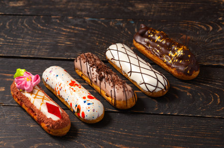 Beautiful delicious french eclairs set with original cream decor on dark wood background. close-up
