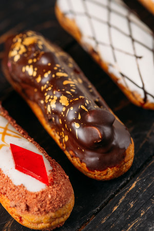 Beautiful delicious French eclairs set with original cream decor on dark wood background. close-up...
