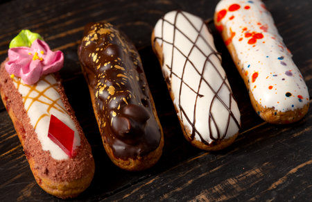 Beautiful delicious french eclairs set with original cream decor on dark wood background.
