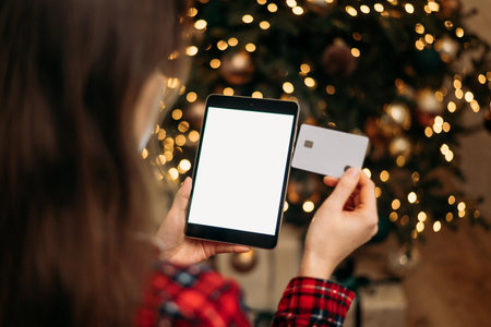 Christmas online shopping, sales and discounts promotions during winter holidays, online shopping at home. Female hands on the tablet with credit card and blurred bokeh lightsの写真素材