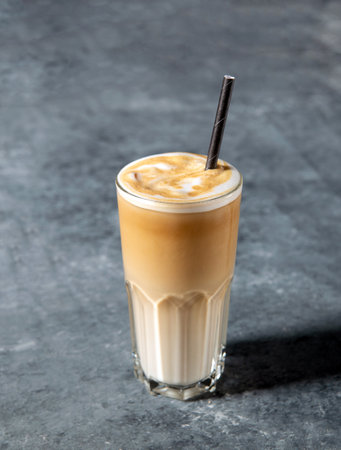 Iced coffee latte in a tall glass with cream or milk and straw on gray background with copy spaceの写真素材