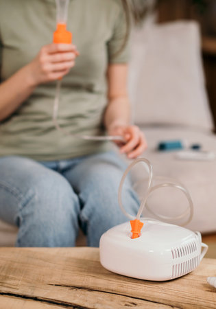 Woman using a nebulizer for respiratory treatment at home, sitting on a couch with medical equipment on the table.の写真素材