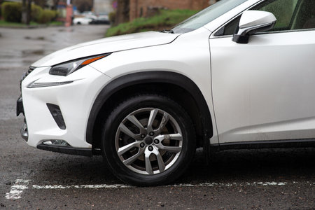 Close-up of a white SUV's wheel and fender on a rainy urban street, highlighting modern automotive style and wet conditions.の写真素材