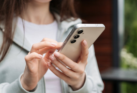 Close-up of hands holding and using a modern smartphone outdoors, showcasing technology and connectivity in daily lifeの写真素材