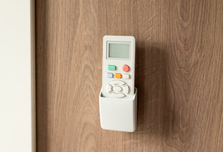 White remote control in a wall holder mounted on a wooden surface, used for air conditioning or home devices.の写真素材