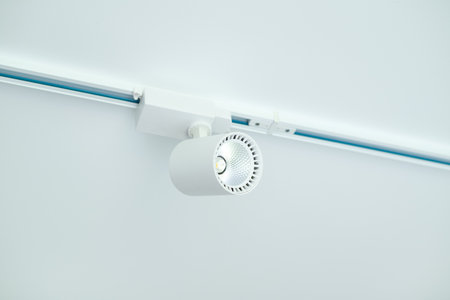 Modern white LED track light fixture mounted on ceiling rail, minimalistic interior lighting solution, close-up view.の写真素材