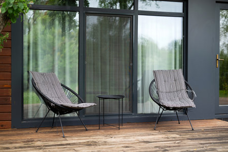 Two modern chairs and a small table on a wooden terrace by glass doors. Minimalistic outdoor seating area for relaxation.の写真素材